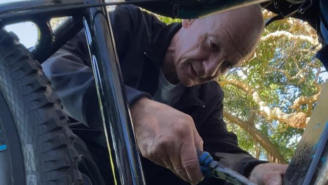 Lane, one of the homeless camping in Carey Park at Southport, fixes his bicycle.