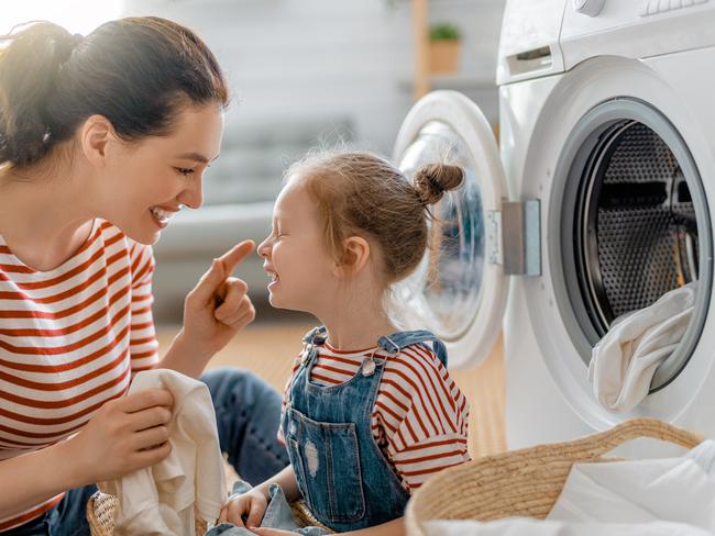 Beautiful young woman and child girl little helper are having fun and smiling while doing laundry at home.