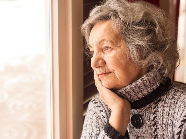 Lonely senior woman looking through window istock image