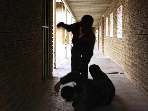 Two school kids fight in a dark passageway of their school, almost silhouette.