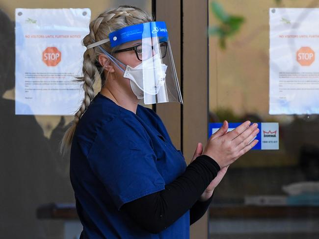 A staff member sanitises her hands outside the Menarock Life aged care facility, where a cluster of some 28 new infections had been reported, in the Melbourne suburb of Essendon on July 14, 2020, as the city battles fresh outbreaks of the COVID-19 coronavirus. - Authorities on July 13 reported 177 new infections in and around Melbourne after the Australian city imposed a six-week lockdown on July 9, with surrounding Victoria state sealed off from the rest of the country in an effort to contain the virus. (Photo by William WEST / AFP)