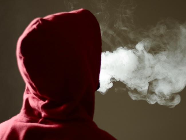 Young male in red hoodie vaping smoking, exhales thick vapor, isolated rear view