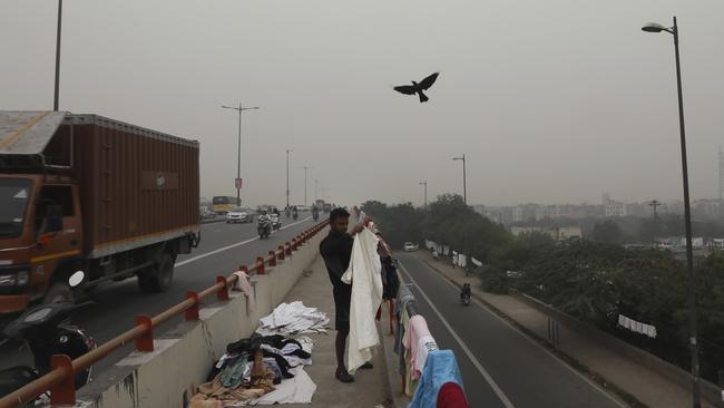 A washerman collects the clothes spread for drying at an overbridge as city is seen enveloped in thick layer of smog in New Delhi, India. Picture: Manish Swarup.