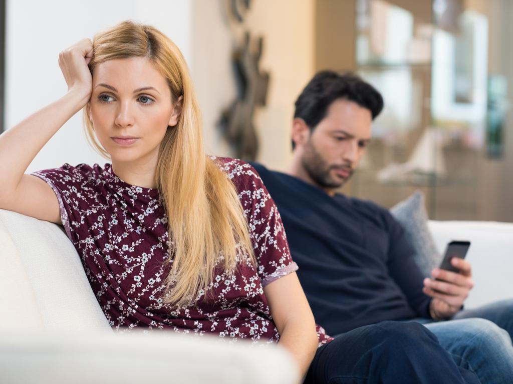 Young woman getting bored while man using phone in the background. Beautiful young woman feeling annoyed as man texting on phone. Young woman after an argument with her boyfriend in their living room.