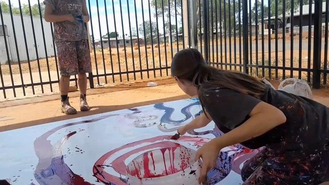 A still taken from video where a non-indigenous employee, Tjala Art manager Rosie Palmer is seen contributing to a painting by Indigenous artist Yaritji Young.