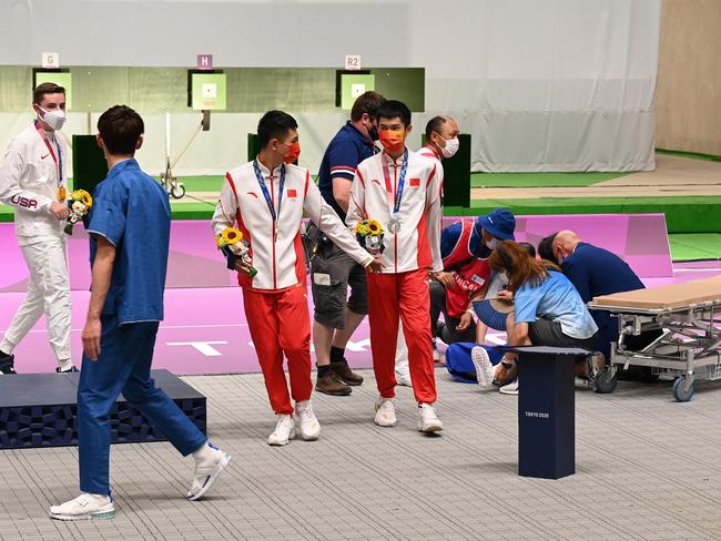 People assist an official who collapsed following the men’s 10m air rifle medal ceremony. Picture: AFP