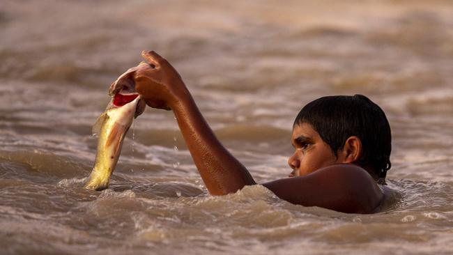 A boy catches a fish by hand at Brewarrina Weir. Picture: Jenny Evans/Getty Images