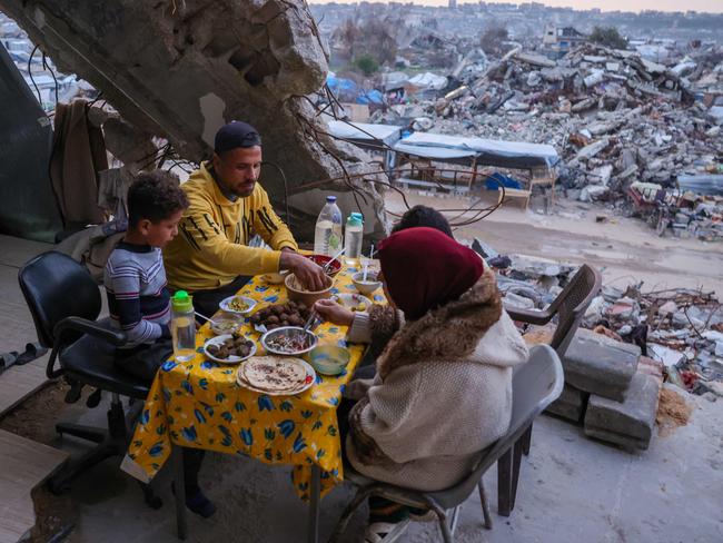 A Palestinian family (C-L) eat an iftar meal, the breaking of the fast, in their destroyed house amid the rubble of buildings in Beit Lahia in the northern Gaza Strip on March 4, 2025, during the Muslim holy fasting month of Ramadan. UN chief Antonio Guterres said he strongly endorsed an Egyptian plan put to Arab leaders at a summit in Cairo on March 4 for Gaza's reconstruction without displacement of its Palestinian inhabitants. (Photo by Bashar TALEB / AFP)