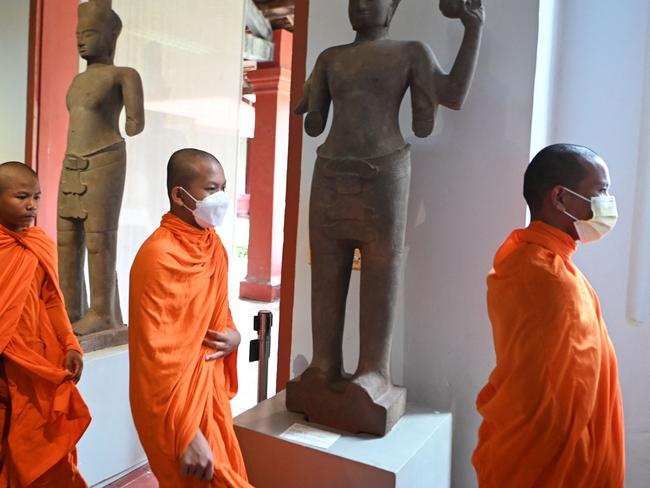 Buddhist monks walk past statues at the National Museum in Phnom Penh on July 13, 2022. (Photo by TANG CHHIN Sothy / AFP)