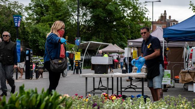 A customer wears a face mask and gloves as she shops at a flower stall at Blackheath Farmers Market in London. Picture: Getty Images.