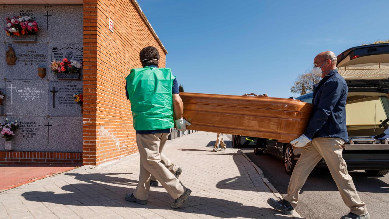 A coronavirus victim’s coffin is taken to a burial in Madrid by workers in masks on Sunday. Picture: Baldesca Samper/AFP