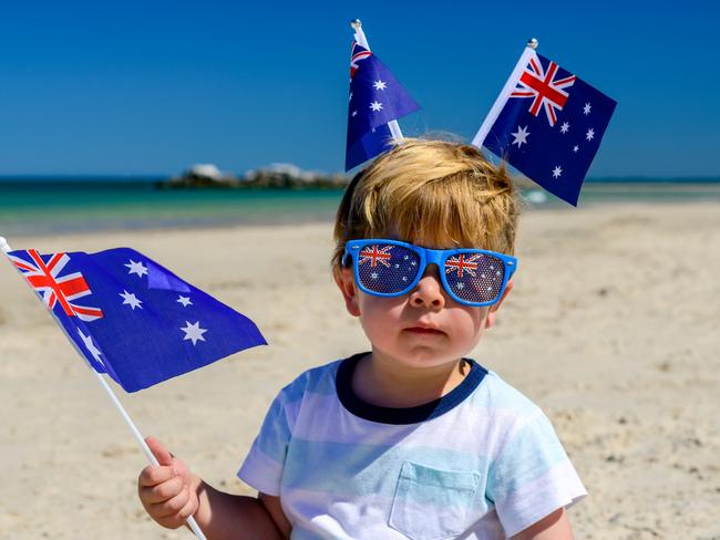 Cute smiling kid with Australian flags sitting on the sand at the beach on Australia Day