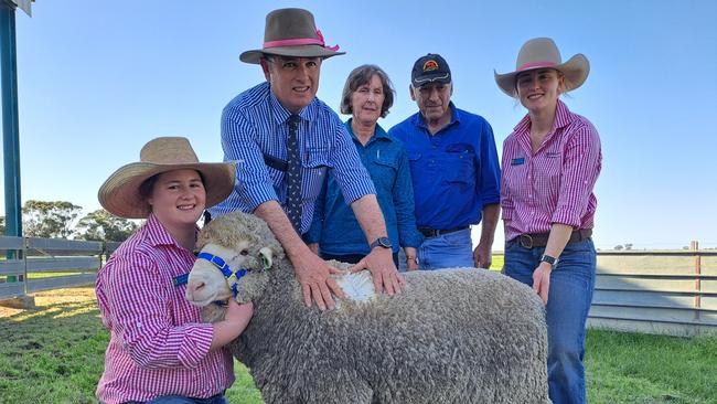 Colin McCrabb shows the wool on the $7000 ram which is held by daughters Amelia and Phoebe, with buyers Debbie and Graham Mott, Yerong Creek.