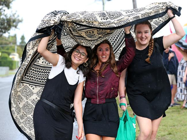 New Years Eve 2018 - Crowds line up to get in to Dudley Page Reserve in Dover Heights to get a prime view of the fireworks. Friends L-R Nivine El-Aawar, Anna Torres and Lea Puls use their picnic rug to take cover from a passing shower. Picture: Toby Zerna