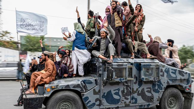 Taliban fighters hold weapons as they ride on a humvee to celebrate their victory day near the US embassy in Kabul, following a turbulent year that saw women's rights crushed and a humanitarian crisis worsen.