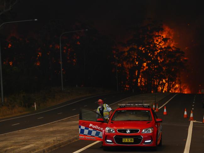 A New South Wales Police officer prepares to flee his roadblock on the Princes Highway near the town of Sussex Inlet on December 31, 2019 in Sydney, Australia. More than 1500 firefighters are currently battling more than 100 blazes across the NSW, with more than 30 fires still yet to be contained. There had been calls for the Sydney New Year's Eve fireworks display to be cancelled due to the ongoing bushfires in NSW, however event organisers have decided to continue as planned following approval from commissioner of the NSW Rural Fire Service Shane Fitzsimmons. Picture: Sam Mooy/Getty