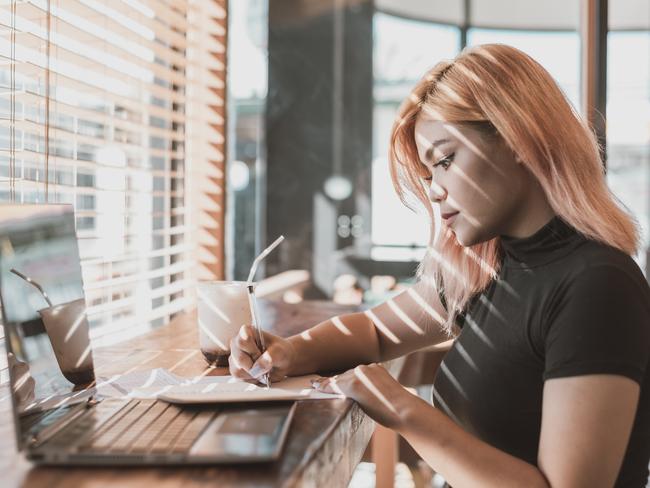 A pretty young focused professional asian woman writing down notes or making a draft. Office worker, businesswoman or freelancer at a coffee shop.