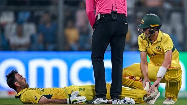 Maxwell (bottom) is helped by his captain Pat Cummins (R) as he battles cramp. Picture: AFP