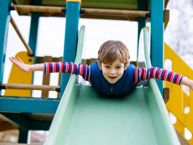 Happy blond kid boy having fun and sliding on outdoor playground. Funny joyful child smiling and climbing on slide. Summer, spring and autumn leisure for active kids. Boy in colorful casual clothes