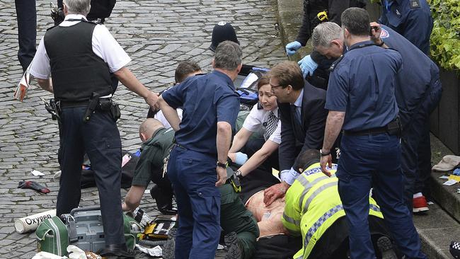 Conservative Member of Parliament Tobias Ellwood, centre, helps emergency services attend to the police officer outside the Houses of Parliament in London.