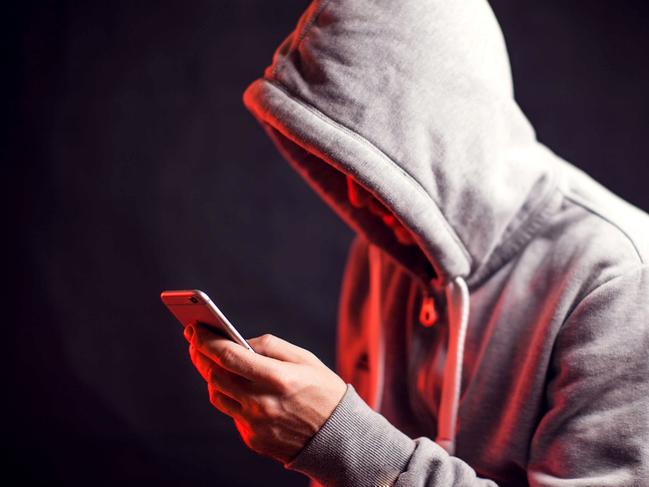Man wearing hoody sweater with mobile phone in hands. Crime and hacking concept; scam generic.