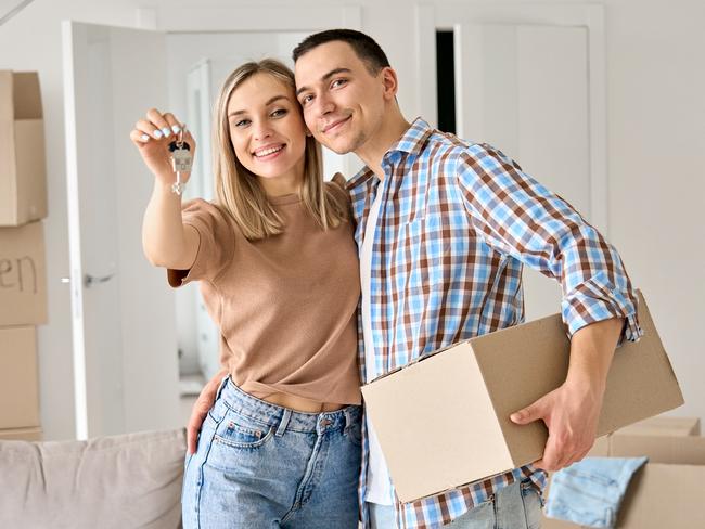 FIRST HOME BUYER Happy young couple home owners holding keys in new home. Smiling independent millennial man and woman first time homeowners carrying boxes on moving day. Mortgage loan, new house ownership concept.