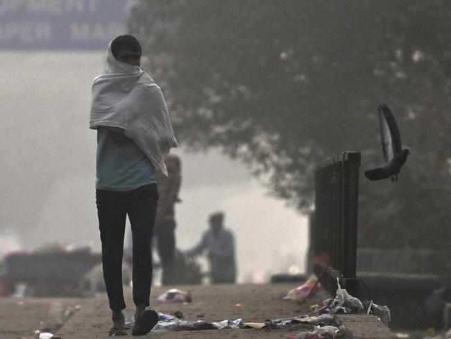 A man covers his face with cloth as he walks past garbage amid smoggy conditions in New Delhi on November 19, 2024. Residents of India's capital New Delhi choked in a blanketing toxic smog on November 18 as worsening air pollution surged past 60 times the World Health Organization's recommended daily maximum. (Photo by Arun SANKAR / AFP)