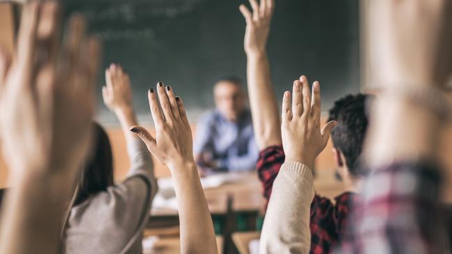 Rear view of group of students raising hands to answer teacher's question in the classroom. Focus is on hands in the middle.Picture: iStock