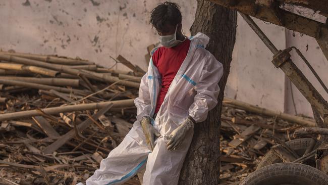 A worker wearing a PPE suit takes a momentary break as people perform the last rites of patients who died of COVID-19 during a mass cremation held at a crematorium in New Delhi, India. Pictire: Anindito Mukherjee/Getty Images