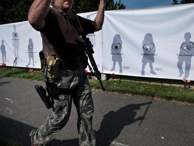 A gun rights advocate carries an assault style rifle past a poster depicting victims of the Sandy Hook Elementary School mass shooting outside the National Rifle Association in Fairfax, Virginia. Picture: AFP