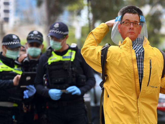 A protester (R) wears a face shield with an image of Victoria's state premier Daniel Andrews on it as speaks to police during an anti-lockdown rally in Melbourne on September 12, 2020, as the city continues to enforce strict lockdown measure to battle a second wave of COVID-19 coronavirus infections. (Photo by William WEST / AFP)