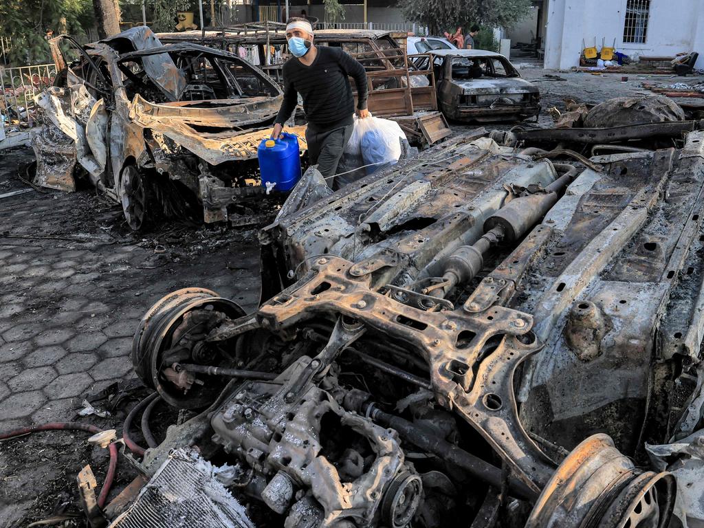 A man walks with salvaged items past destroyed vehicles at the site of the Ahli Arab hospital in central Gaza on October 18. Picture: AFP