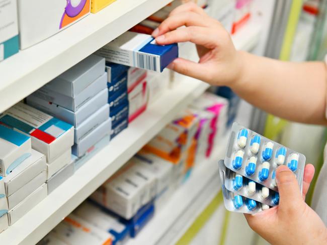 Pharmacist holding medicine box and capsule pack in pharmacy drugstore.