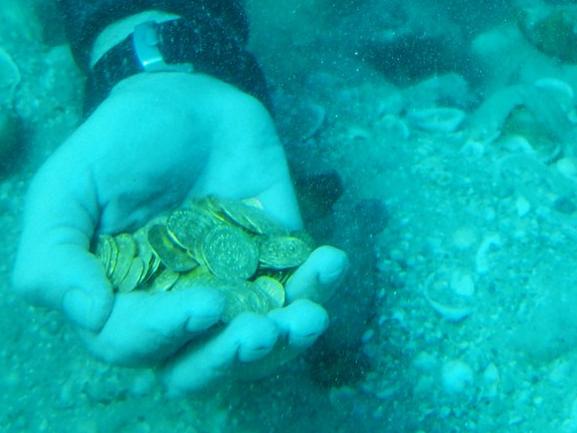 A handout picture released by Israel's Antiquities Authority on February 17, 2015 shows a scuba diver holding in his hand some of the gold coins recently found on the seabed in the ancient harbour in the Israeli town of Caesarea. Scuba divers have discovered the largest trove of gold coins ever found off Israel's Mediterranean coast -- about 2,000 pieces dating back more than 1,000 years, the country's antiquities authority said. AFP PHOTO / ISRAEL ANTIQUITIES AUTHORITY / KOBI SHARVIT === RESTRICTED TO EDITORIAL USE - MANDATORY CREDIT "AFP PHOTO / ISRAEL ANTIQUITIES AUTHORITY / KOBI SHARVIT" - NO MARKETING NO ADVERTISING CAMPAIGNS - DISTRIBUTED AS A SERVICE TO CLIENTS ===