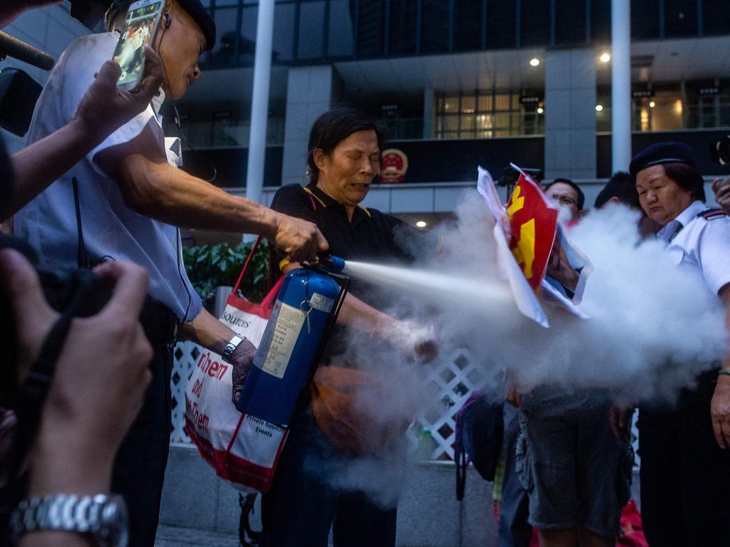 A security guard extinguishes a burning portrait of Chinese leader Xi Jinping held by a pro-democracy activist during a protest march by thousands in Hong Kong. Picture: AFP