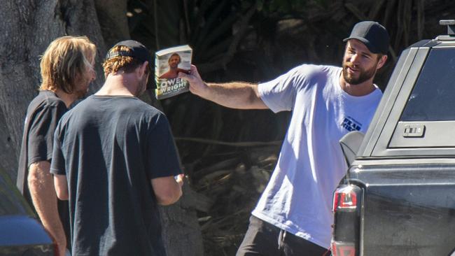 Surf buddies, L-R: Owen Wright, Chris and Liam Hemsworth, with Liam holding a copy of Owen’s memoir. Picture: BYRON