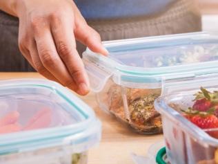 A woman meal preps in the kitchen. She is putting black berries, strawberries, peas, and nuts into clear glass food storage containers with lids.