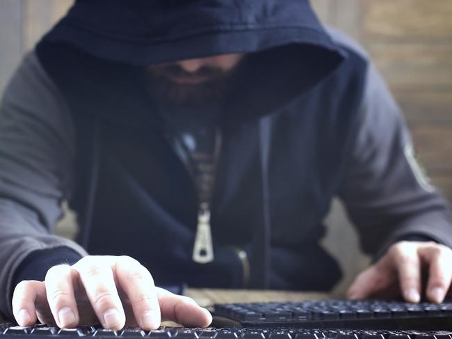 hacker in the black hood in a room with wooden walls makes cybercrime istock image