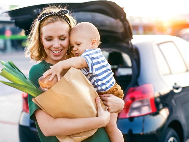 Beautiful young mother with her little baby son in front of a supermarket, holding paper shopping bag. Woman with a boy standing by the car.Istock image for wellbeing in Gold Coast Eye