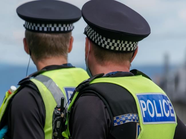 20th June 2020: Rear view of two male Police Scotland officers on duty in Edinburgh, during a Black Lives Matter demonstration in St Andrew Square, during the Coronavirus pandemic. One officer is wearing protective rubber gloves. Both officers are wearing high visibility jackets with their police uniforms, with the police logo on the back. They are standing looking down the street, keeping surveillance of the crowds. They have handheld radios attached to their jackets to communicate with colleagues.