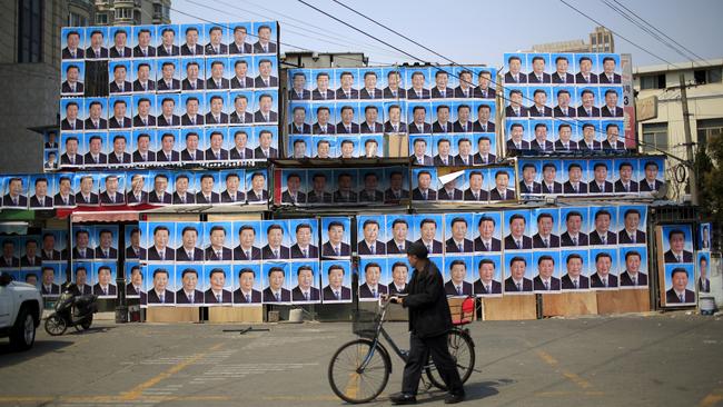 A man wheels a bicycle past a building covered in hundreds of posters of Chinese President Xi Jinping in Shanghai. Picture: Reuters