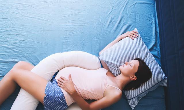Beautiful pregnant woman relaxing or sleeping with tummy supporting pillow at bed. Young mother waiting of a baby. Concept of pregnancy, maternity, health care, gynecology, medicine.