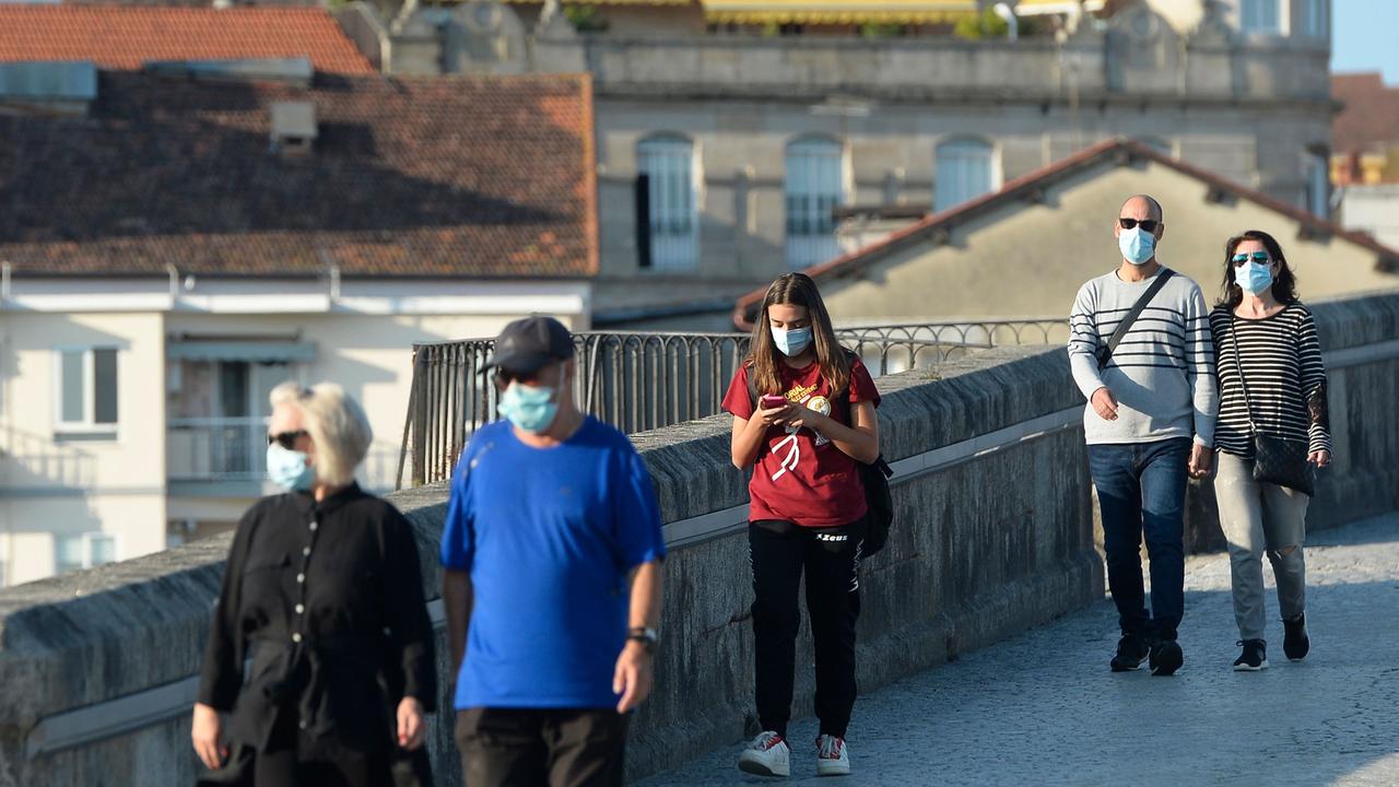 People wearing face mask walk over the Roman Bridge in downtown Ourense, northwestern Spain. Picture: Miguel Riopa/AFP.