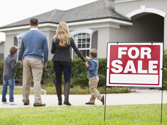 Family with two boys (4 and 6 years) standing in front of house with FOR SALE sign in front yard.  Focus on sign.