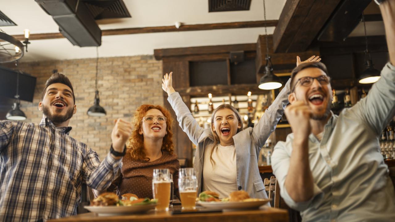 Four young people watching a football game in pub cheering. Photo: iStock.