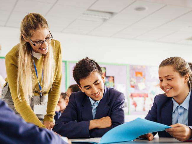 Female teacher with her students. Teenage students sitting around a table while their teacher stands over them smiling. Low angle view point