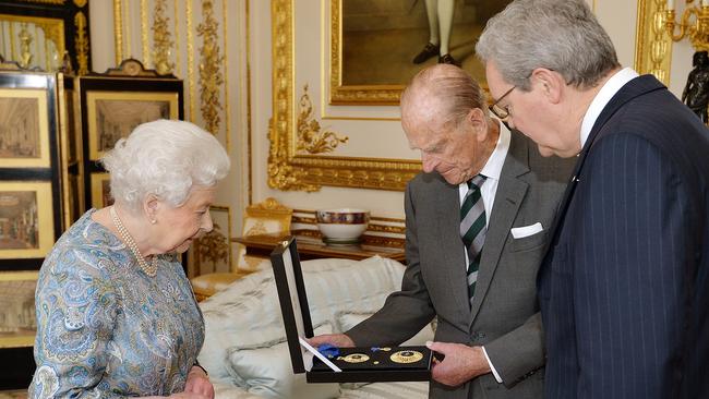 Queen Elizabeth II (L) presents Prince Philip, Duke of Edinburgh (C) with the Insignia of a Knight of the Order of Australia as Australian High Commissioner Alexander Downer (R) looks on.