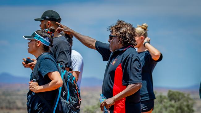 Anangu man Rueben Burton points toward Uluru in the distance, alongside Port Adelaide Football Club staff and players. Credit: Michael Sullivan.