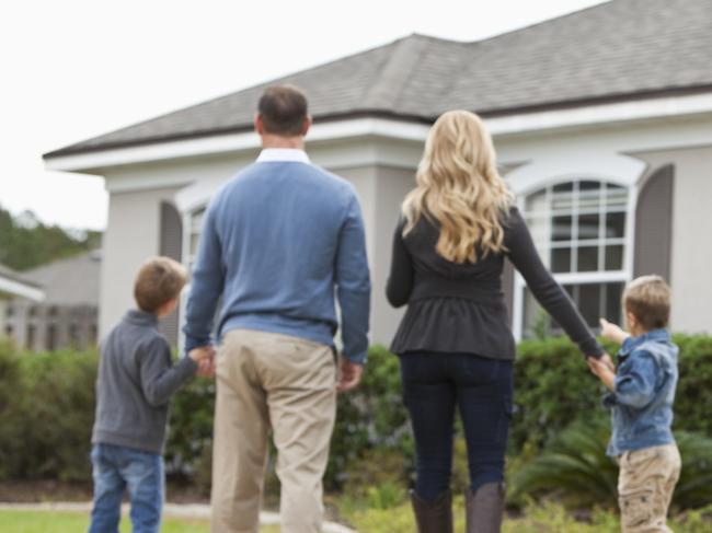 Family with two boys (4 and 6 years) standing in front of house with FOR SALE sign in front yard.  Focus on sign.