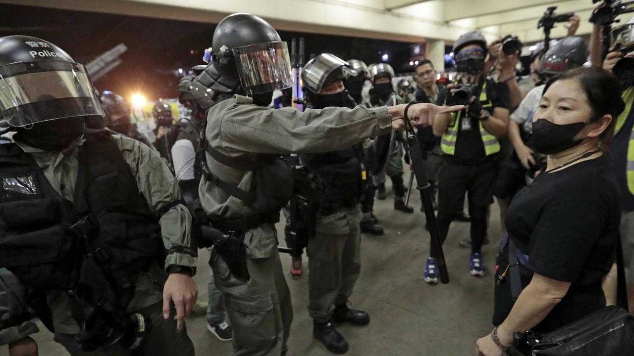 Police in riot gear ask a woman to take off her mask outside a train station in Hong Kong. Picture: AP